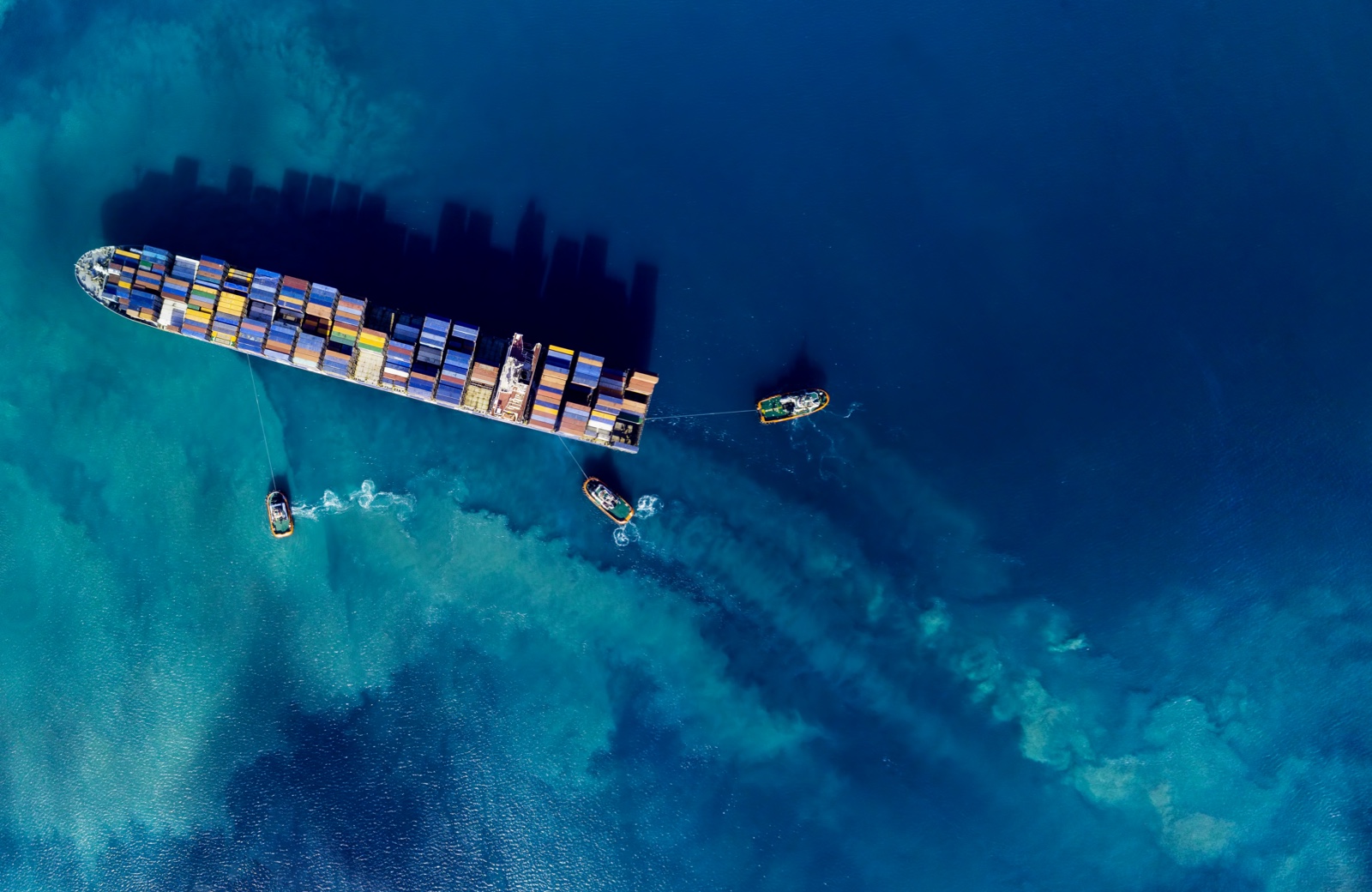 Aerial view of container ship in ocean with smaller guide boat attached from above